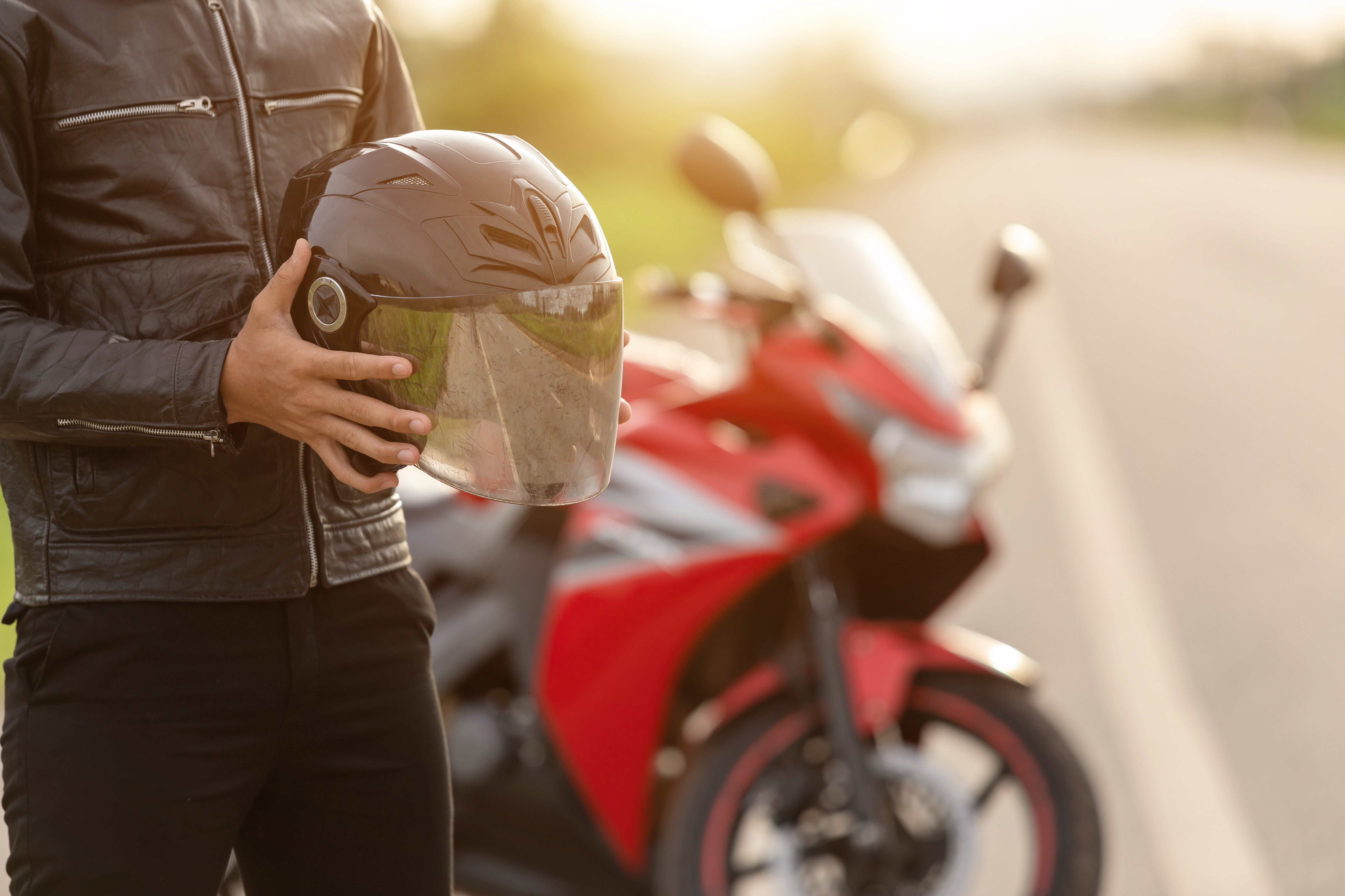 motorcyclist wear leather jacket and holding helmet on the road. Safe ride and transportation concept